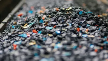 Un homme d'affaires portant des lunettes et une chemise à carreaux bleus, regardant l'objectif avec assurance sur un fond neutre.