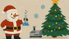 Ein fröhlicher Weihnachtsmann hält einen Erlenmeyer-Kolben neben einen geschmückten Weihnachtsbaum und einen NETZSCH Gerätes.