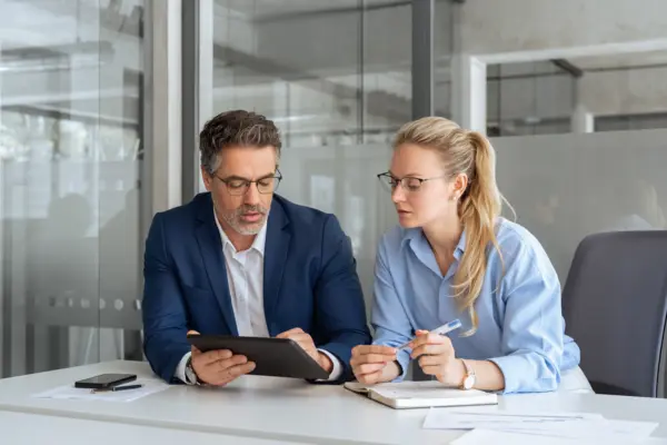Zwei Fachleute arbeiten am Tisch zusammen, analysieren Daten auf einem Tablet und tauschen Ideen aus.