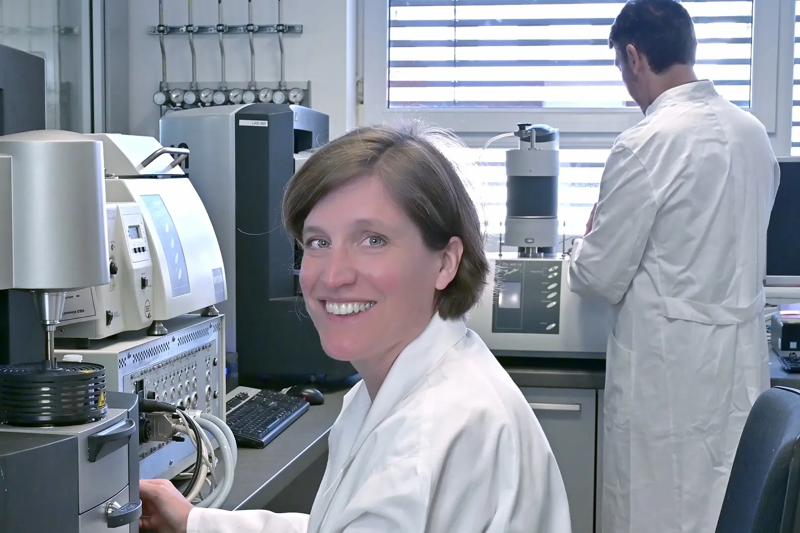 A lab technician smiles while operating advanced thermal analysis equipment in a modern applications laboratory.