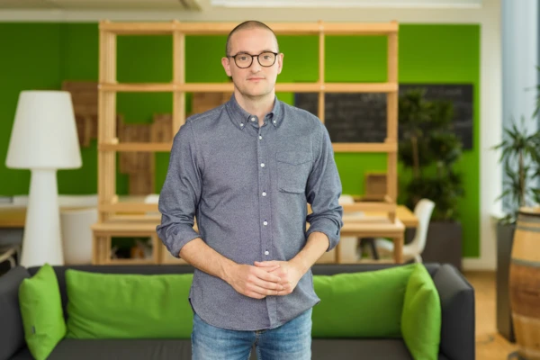 Professional man in a casual blue shirt stands confidently in a modern office space with green accents.