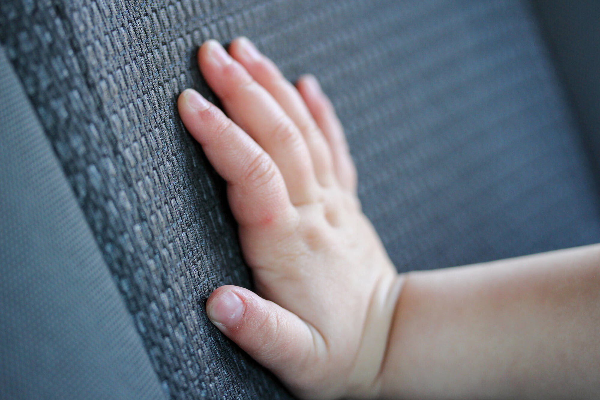 La mano di un bambino tocca delicatamente un tessuto automobilistico grigio, evidenziando i materiali utilizzati nei test di sicurezza degli interni dei veicoli.