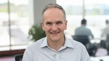 Professional man with glasses wearing a blue plaid shirt, looking confidently at the camera against a neutral background.