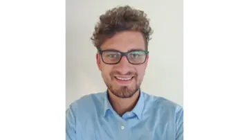 رجل ذو مظهر مهني يرتدي نظارات وقميصًا أزرقًا منقوشًا، ينظر بثقة إلى الكاميرا أمام خلفية محايدة.