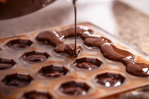 Il ricco cioccolato fuso viene versato in uno stampo a forma esagonale per creare eleganti forme di cioccolato per i dolci.