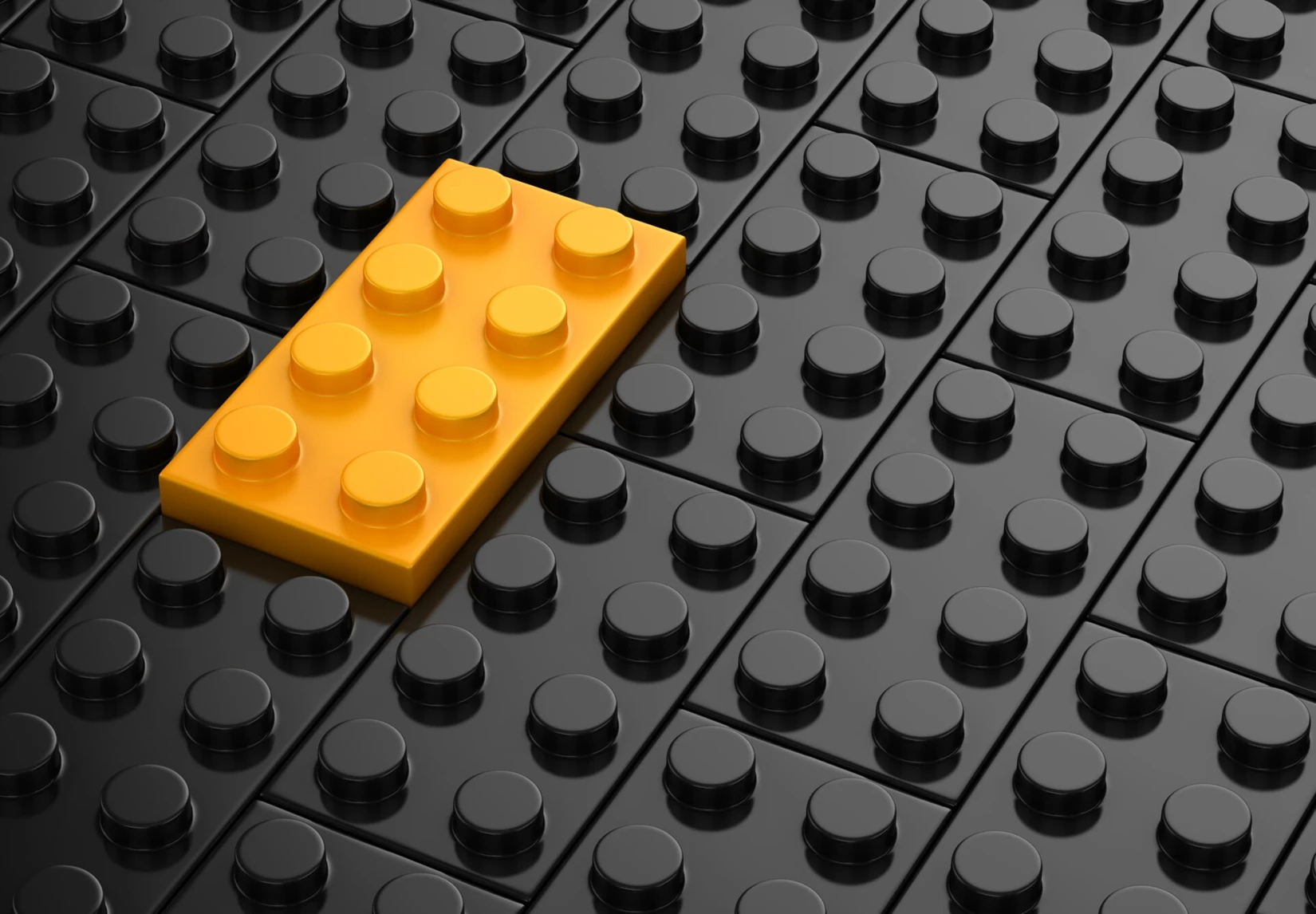 A single yellow LEGO brick stands out against a textured backdrop of black LEGO bricks, symbolizing creativity and individuality.