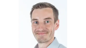 Professional man with glasses wearing a blue plaid shirt, looking confidently at the camera against a neutral background.
