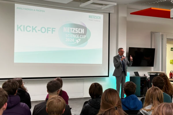 Оратор се обръща към аудиторията по време на откриващото събитие на NETZSCH Science Cup, с логото и слайда на презентацията.
