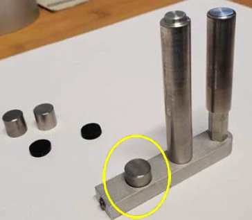 Apparecchio di prova per metalli con componenti cilindrici e small dischi metallici, che evidenziano un pezzo circolare centrale per l'analisi.