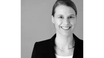Professionele man met bril draagt een blauw geruit overhemd en kijkt zelfverzekerd naar de camera tegen een neutrale achtergrond.