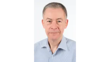 Een zakelijke man met een bril, gekleed in een blauw geruit overhemd, die zelfverzekerd in de camera kijkt tegen een neutrale achtergrond.