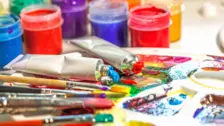 Bright artist paints squeezed from tubes onto a palette with colorful brushes and jars of paint in the background.