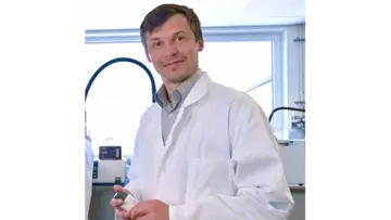 Profesionální muž s brýlemi v modré kostkované košili, který se sebevědomě dívá do kamery na neutrálním pozadí.
