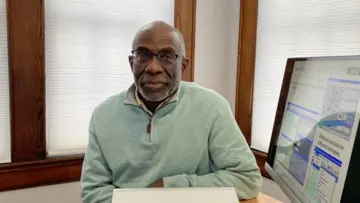 Professional man with glasses wearing a blue plaid shirt, looking confidently at the camera against a neutral background.