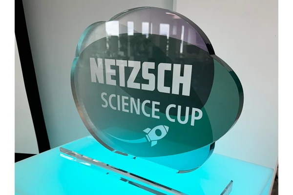 NETZSCH Трофей за купата на науката, поставен върху светеща основа, символизиращ иновациите и творчеството в научното образование.