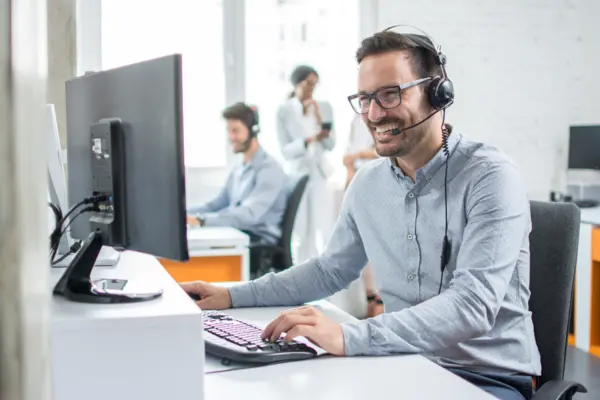 Mitarbeiter mit Headset lächelt am Computer in einem modernen Büro, ideal für Kundenservice und technischen Support bei NETZSCH.