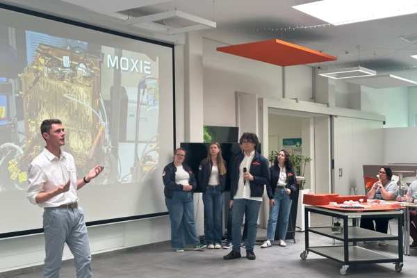 Students pitch innovative lab designs during the NETZSCH Science Cup, with a "MOXIE" presentation in the background.