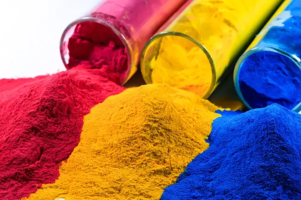 Bright red, yellow, and blue polyurethane powder coatings spilling from glass containers, illustrating pigment quality for automotive applications.