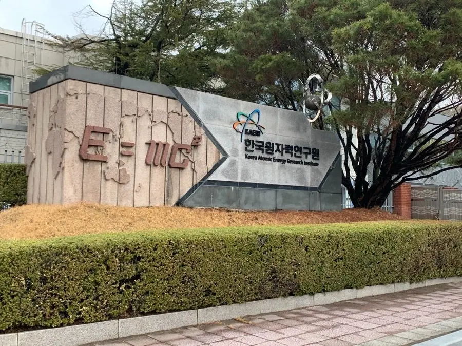 Entrance sign of Korea Atomic Energy Research Institute (KAERI) with scientific symbols and surrounding greenery under overcast sky