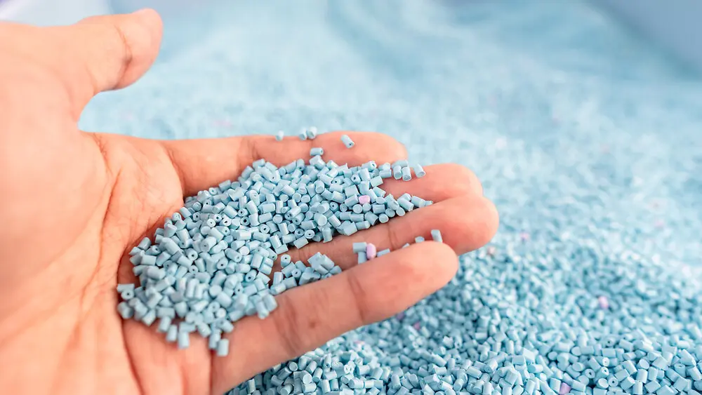 Mão segurando grânulos de polímero azul small, utilizados para análise térmica e testes de materiais de polipropileno, fornecidos por NETZSCH.
